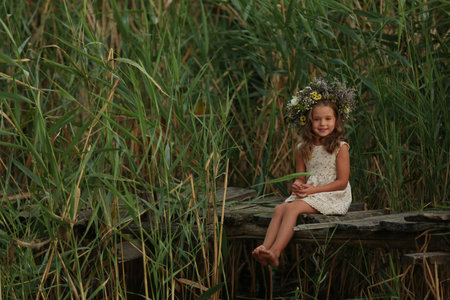 Cute little girl wearing wreath made of beautiful flowers on wooden bridgeの写真素材