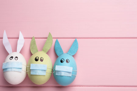 Dyed eggs with bunny ears in protective masks on pink wooden background, flat lay and space for text.の写真素材