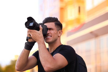 Photographer taking picture with professional camera on city street at sunsetの写真素材
