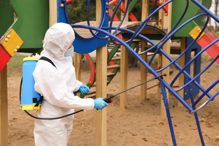 Woman wearing chemical protective suit with disinfectant sprayer on playground. Preventive measure during coronavirus pandemicの写真素材