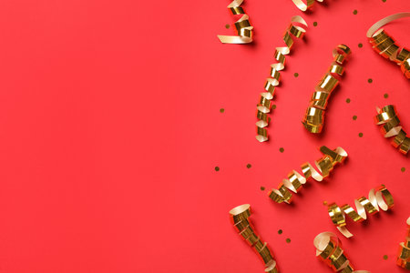 Shiny golden serpentine streamers and confetti on red background, flat lay. Space for textの写真素材