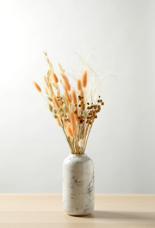 Dried flowers in vase on table against light backgroundの写真素材