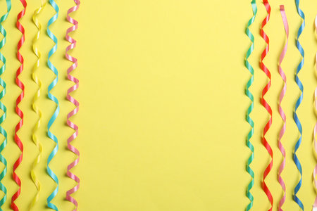Colorful serpentine streamers on yellow background, flat lay. Space for textの写真素材