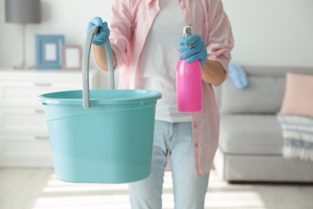 Woman holding bucket and bottle of cleaning product at home, closeupの写真素材