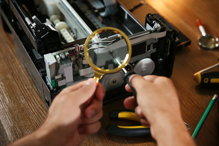 Repairman with magnifying glass and screwdriver fixing modern printer, closeupの写真素材