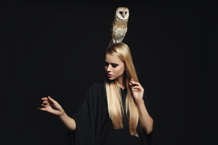 Witch in black mantle with owl on dark background. Scary fantasy characterの写真素材