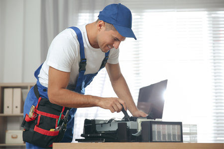Repairman with screwdriver fixing modern printer in officeの写真素材