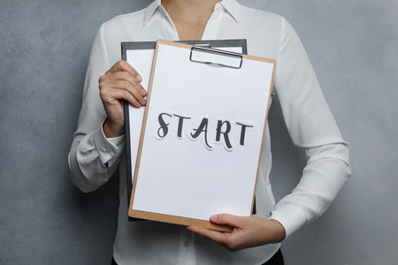 Woman holding clipboards with word Start on grey background, closeupの写真素材