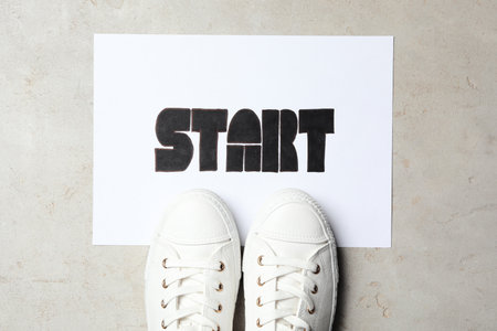 Sheet of paper with word Start and stylish sneakers on grey table, flat layの写真素材