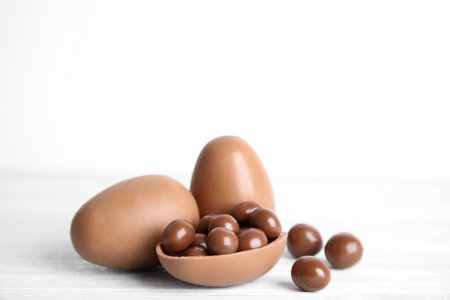 Whole and broken chocolate eggs with candies on white wooden tableの写真素材