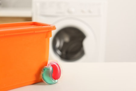 Laundry container and washing detergent capsule on table indoors. Space for textの写真素材