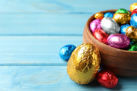 Chocolate eggs wrapped in colorful foil on light blue wooden table. Space for textの写真素材