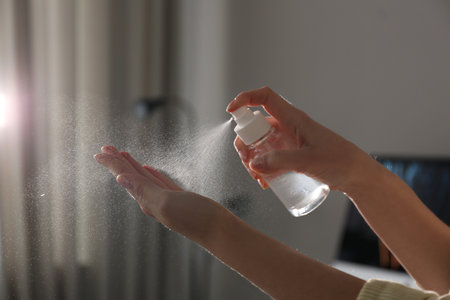 Woman spraying antiseptic onto hand indoors, closeup