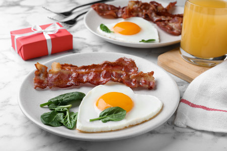 Romantic breakfast with fried bacon and heart shaped egg on white marble table. Valentine's day celebrationの写真素材