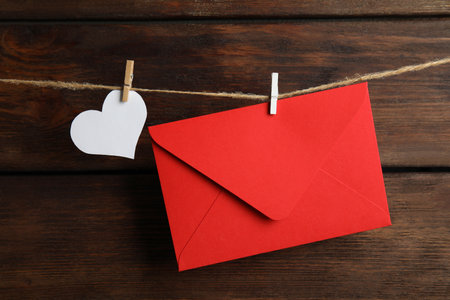 Red envelope and paper heart hanging on twine against wooden background. Love letterの写真素材