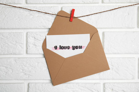 Envelope with I Love You card hanging on twine near white brick wallの写真素材