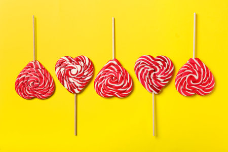 Sweet heart shaped lollipops on yellow background, flat lay. Valentine's day celebrationの写真素材