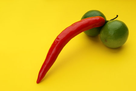 Chili pepper and limes symbolizing male sexual organ on yellow background. Potency problemの写真素材