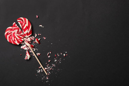 Broken heart shaped lollipop on black background, top view with space for text. Relationship problems conceptの写真素材