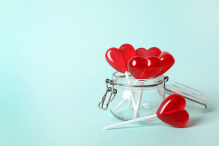 Sweet heart shaped lollipops in glass jar on light blue background, space for text. Valentine's day celebrationの写真素材