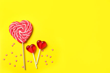 Sweet heart shaped lollipops and sprinkles on yellow background, flat lay with space for text. Valentine's day celebrationの写真素材