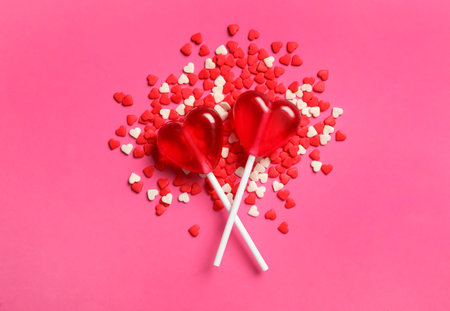 Sweet heart shaped lollipops and sprinkles on pink background, flat lay. Valentine's day celebrationの写真素材