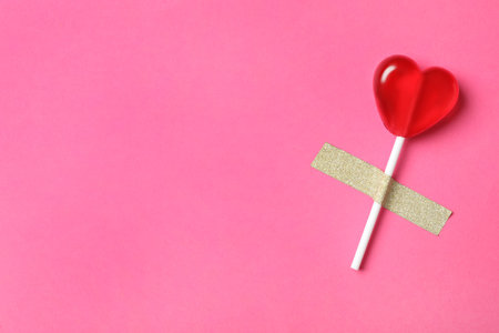 Sweet heart shaped lollipop taped to pink background, top view with space for text. Valentine's day celebrationの写真素材