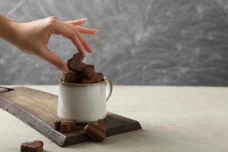 Woman taking heart shaped chocolate candy from cup at light table, closeup. Space for textの写真素材
