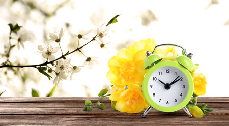 Alarm clock and spring flowers on wooden table, space for text. Time changeの写真素材