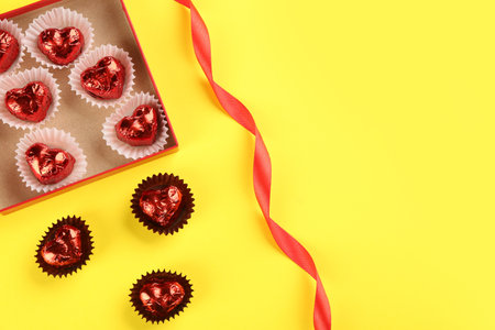 Heart shaped chocolate candies and ribbon on yellow background, flat lay. Space for textの写真素材