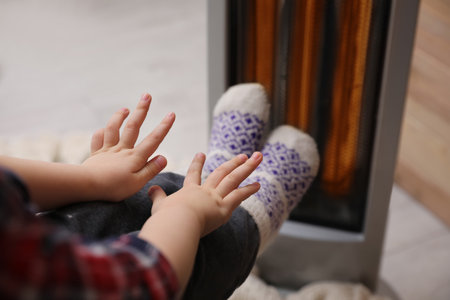 Little kid warming near electric heater at home, closeupの写真素材