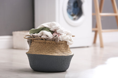 Wicker basket with dirty laundry on floor indoors, space for textの写真素材
