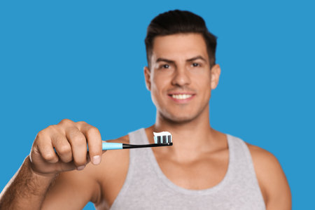 Man holding toothbrush with paste against blue background, focus on handの写真素材