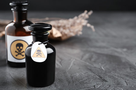Glass bottles of poison with warning signs on grey stone table. Space for textの写真素材
