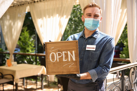 Waiter holding OPEN sign in restaurant. Catering during coronavirus quarantine