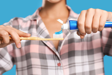 Woman applying toothpaste on brush against blue background, closeupの写真素材