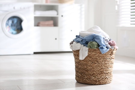 Wicker basket with dirty laundry on floor indoors, space for textの写真素材