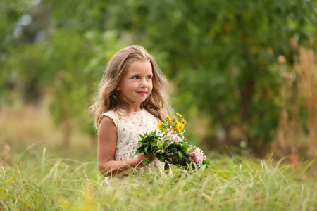 Cute little girl holding wreath made of beautiful flowers in the fieldの写真素材