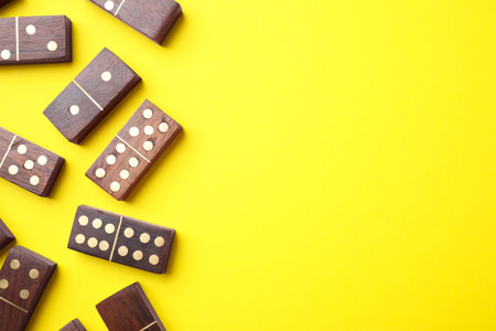 Wooden domino tiles on yellow background, flat lay. Space for textの写真素材