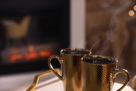 Golden cups with hot drinks against fireplace, closeup. Space for textの写真素材
