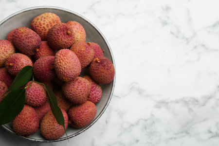 Fresh ripe lychee fruits in bowl on white marble table, top view. Space for textの写真素材