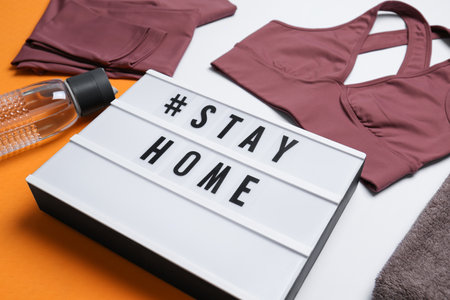 Stylish sportswear, yoga mat and light box with hashtag Stay at Home on white background, closeup.