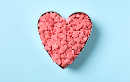 Pink sprinkles in heart shaped cookie cutter on light blue background, top viewの写真素材
