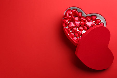 Box with heart shaped chocolate candies on red background, flat lay. Space for text