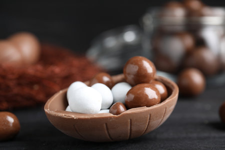 Half of tasty chocolate egg with candies on black wooden table, closeup. Space for textの写真素材