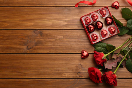 Heart shaped chocolate candies and bouquet on wooden table, flat lay. Space for textの写真素材