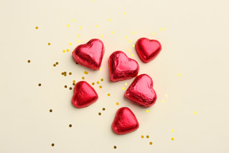 Heart shaped chocolate candies and glitter on beige background, flat layの写真素材