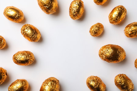 Frame of chocolate eggs wrapped in golden foil on white background, flat lay. Space for textの写真素材