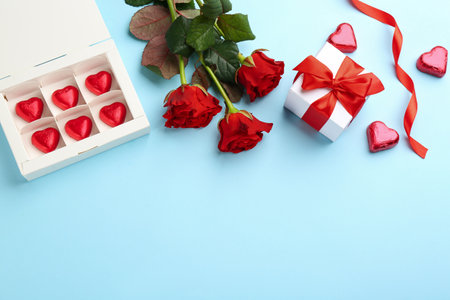 Heart shaped chocolate candies, gift box and bouquet on light blue background, flat lay. Space for textの写真素材