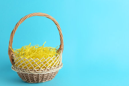 Easter basket with yellow paper filler on light blue background, space for textの写真素材